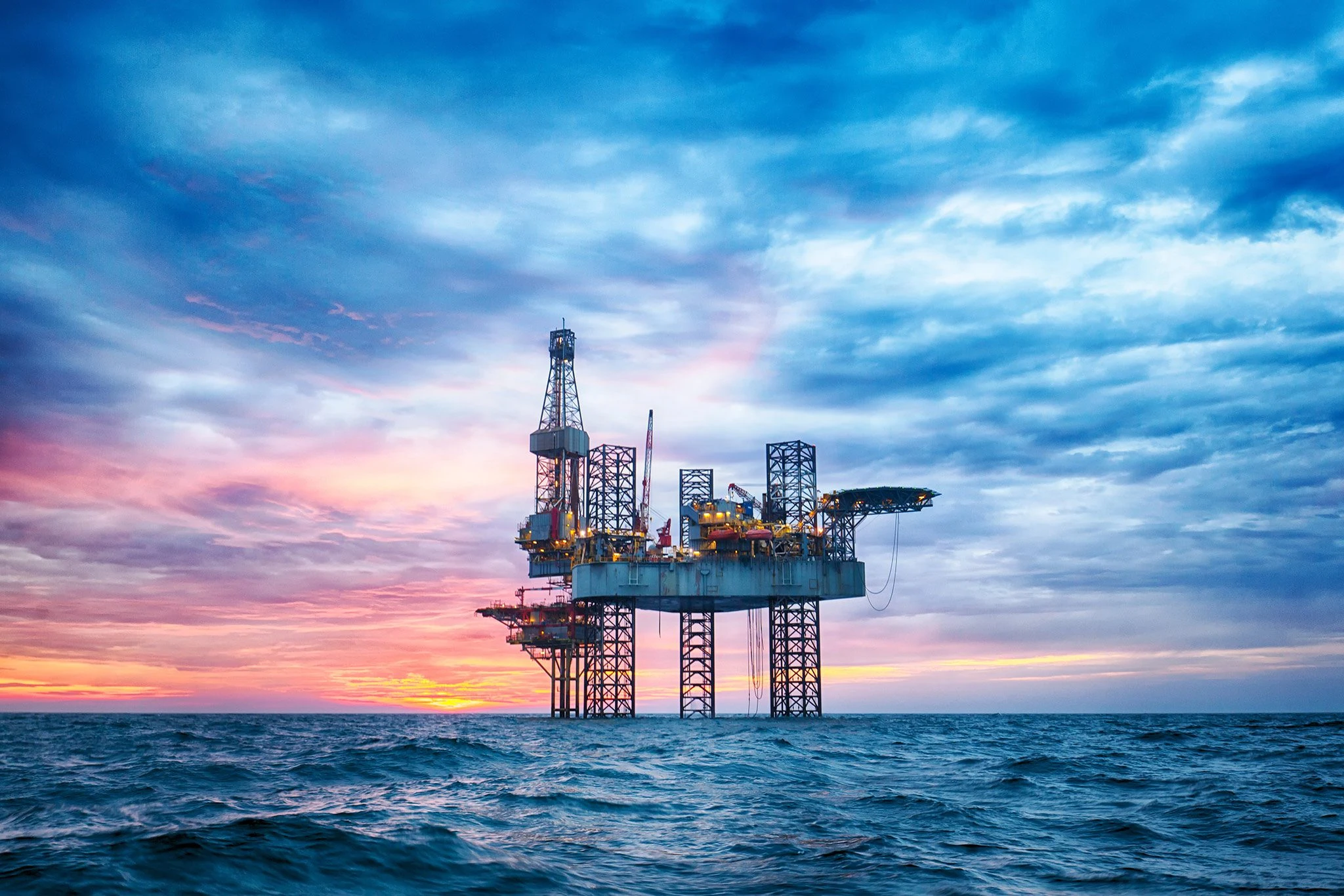 An offshore drilling platform at sunset beneath blue and pink clouds.